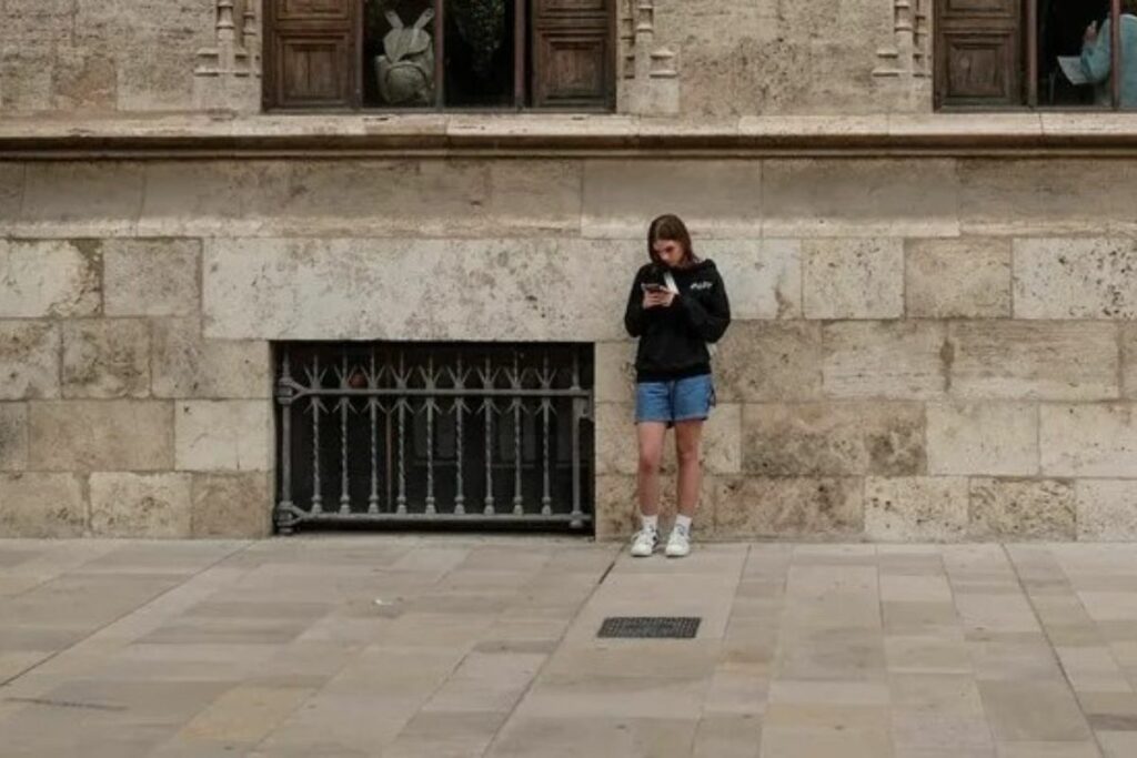 Joven mira su teléfono móvil ante el edifico de La Lonja, en el centro de Valencia. Manuel Bruque/EFE